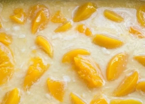 Delicious peach cobbler in a baking dish topped with scoop of ice cream.