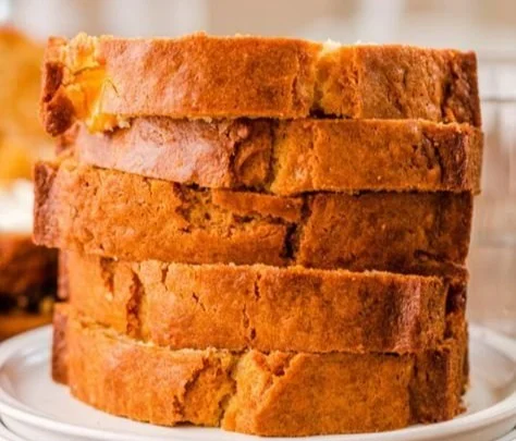 A slice of homemade peach bread surrounded by fresh peaches and a rustic setting.