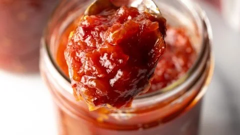 Sweet and tangy tomato jam in a jar with fresh tomatoes on a wooden table