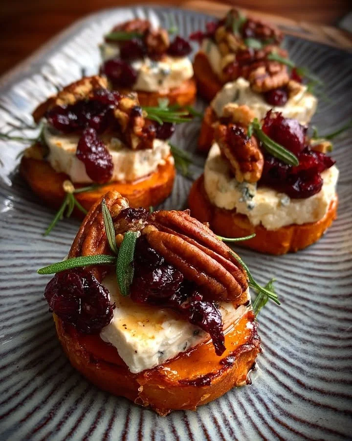 Sweet potato rounds topped with brie, cranberry, and pecans on a plate.