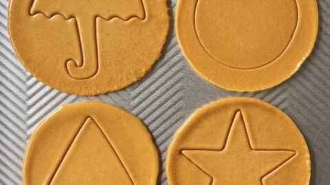 Homemade Dalgona Candy shaped in various designs on a wooden tray