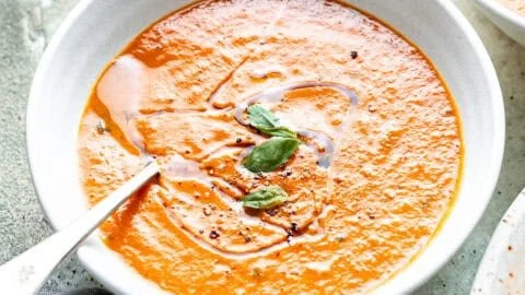 Bowl of easy homemade roasted tomato soup with fresh basil and crusty bread