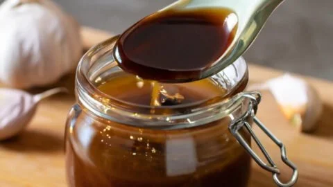 Homemade honey garlic sauce in a glass bowl with ingredients around it.