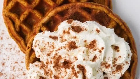 Keto pumpkin chaffles topped with whipped cream and pumpkin seeds