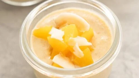 Creamy peach blended chia seed pudding in a bowl topped with fresh peaches