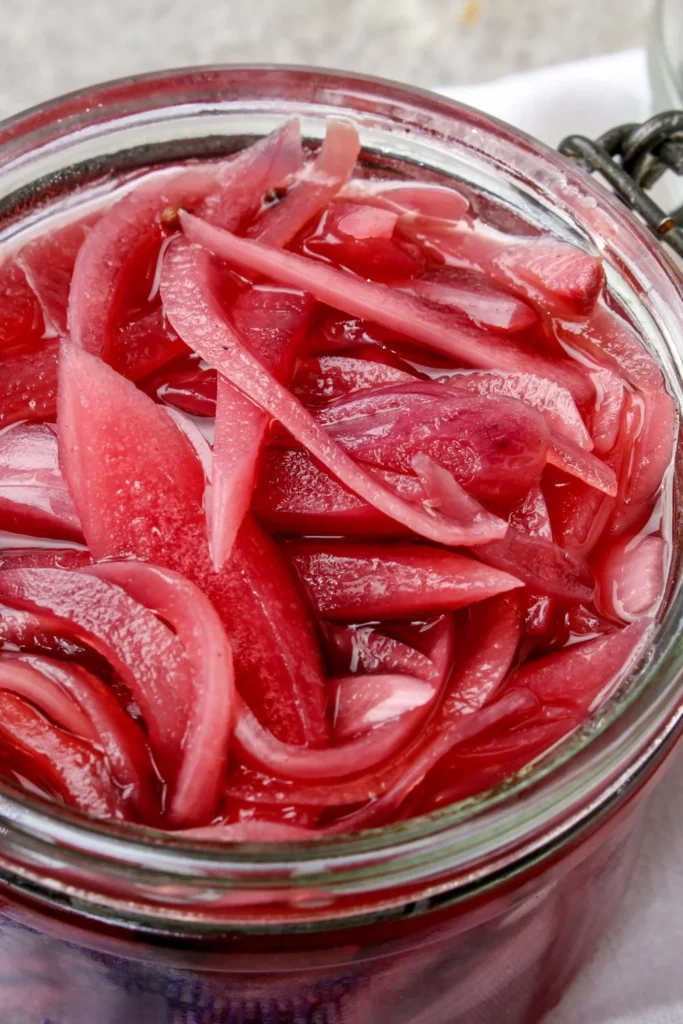 Homemade pickled onions in a glass jar with fresh herbs