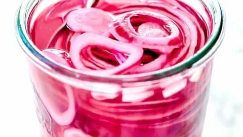 Jar of pickled red onions on a wooden table, ready to enhance meals.