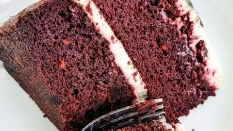 A slice of protein red velvet cake topped with cream cheese frosting