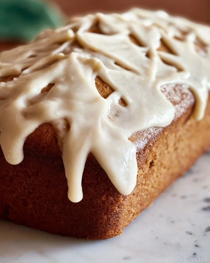 Delicious pumpkin bread with browned butter maple frosting on a rustic wooden table.