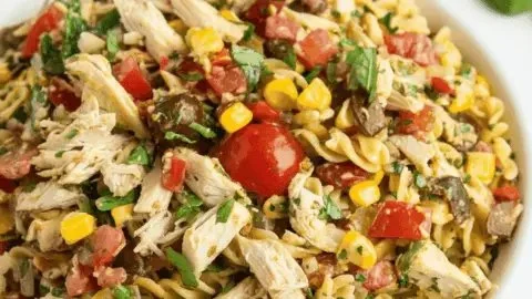 A vibrant bowl of summery chicken pasta salad with fresh vegetables and dressing.