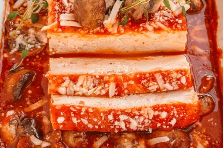 Baked tofu with sautéed mushrooms on a plate, garnished with herbs