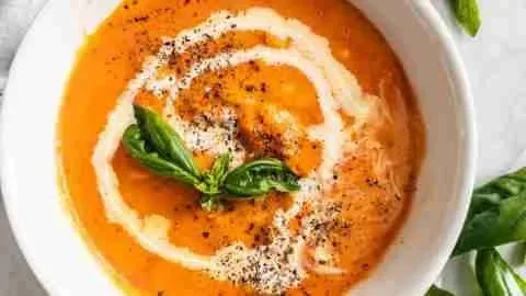 Bowl of creamy roasted tomato soup garnished with basil and served with crusty bread.