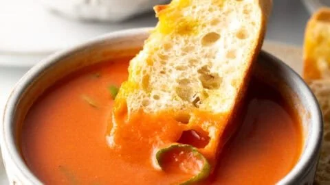 Bowl of easy tomato soup garnished with basil and served with crusty bread