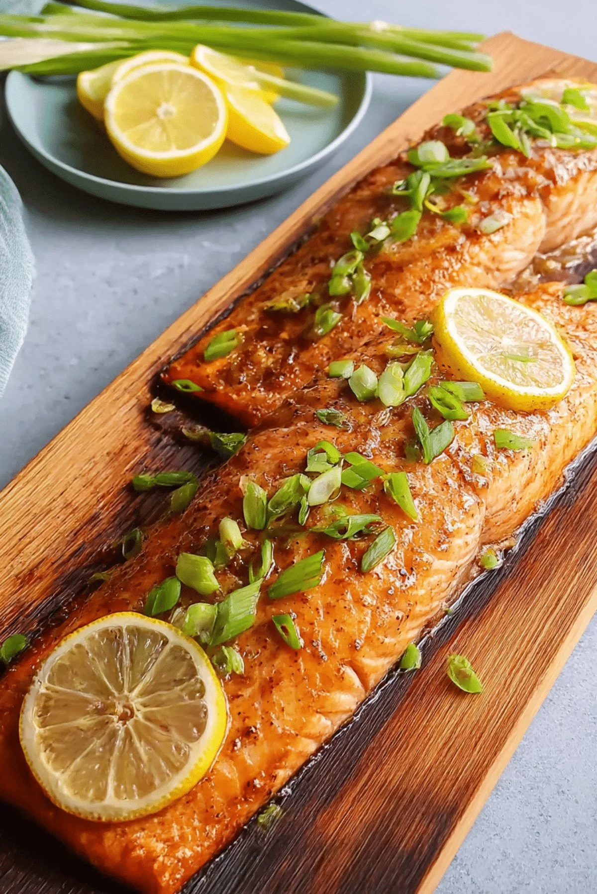 Grilled cedar planked salmon with herbs and lemon garnish on a wooden board.