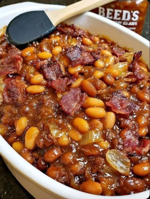 A bowl of Cowboy Baked Beans garnished with herbs, ready to serve at a barbecue
