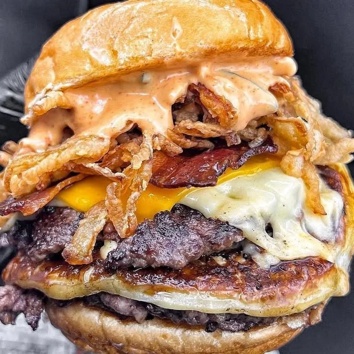 Juicy burger served on a wooden table with fresh ingredients and condiments.