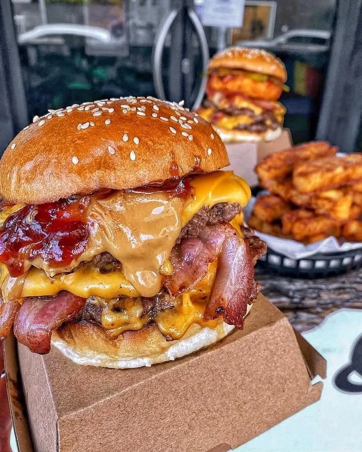 A jar of peanut butter with a spoon surrounded by peanut butter lovers' treats.